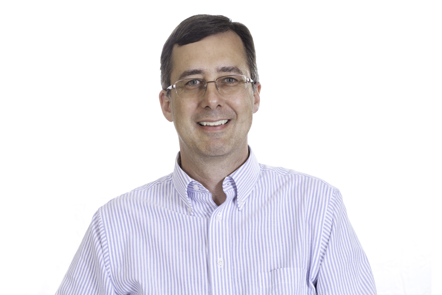 This Brian Charles Steel photo is a headshot of a white gentleman in a dress shirt with white and blue stripes.  He has brown straight hair that is combed to the left.  The gentleman is wearing glasses and a smile.  He is centered in the frame, and the background is completely white.  He is lit with a slight Rembrandt style. 